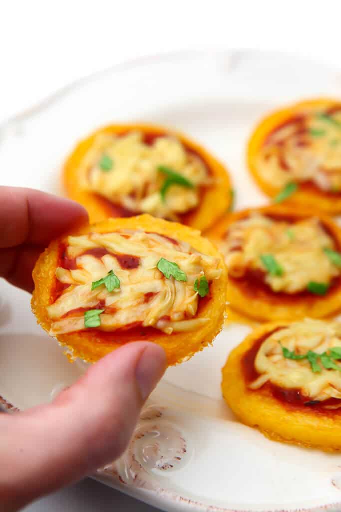 A hand taking a polenta pizza bite off of a plate.