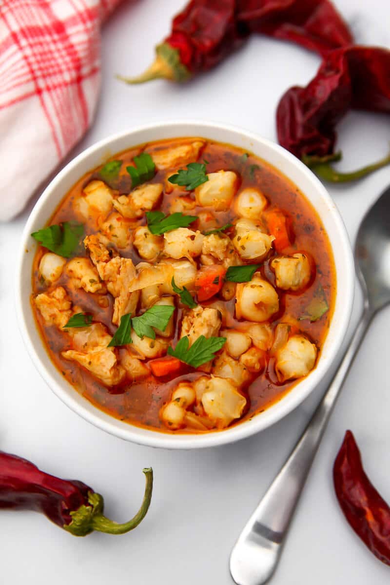 A top view of a bowl of pasole with red chile pods around it.