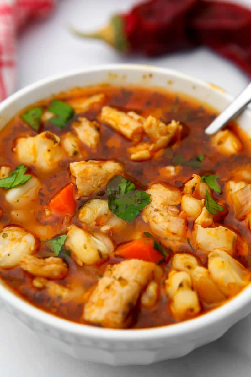 A close up of a bowl of vegan posole with red chiles in the background.