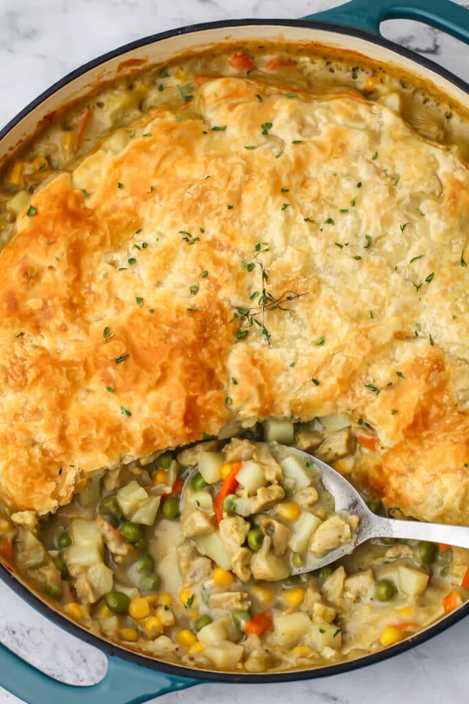 The top view of a cooked vegan pot pie with puff pastry topping with a spoonful taken out.