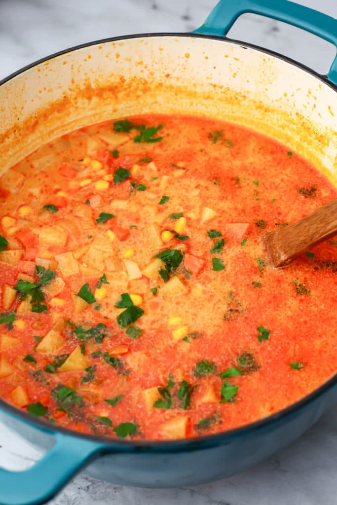 A large pot of vegan potato corn chowder in a large blue soup pot.