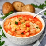 A white bowl filled with vegan potato corn chowder with potatoes and parsley around it.