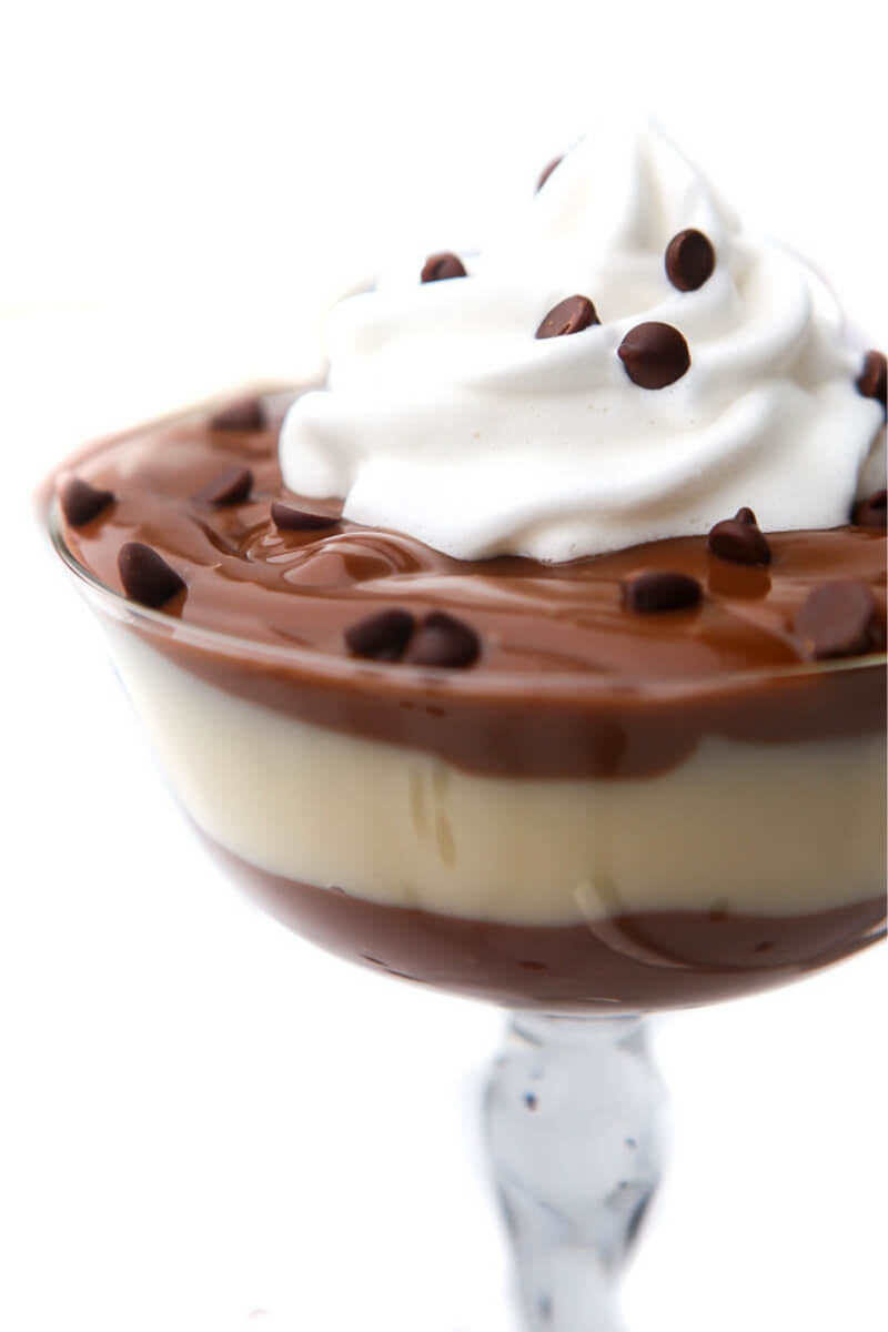 Vegan chocolate and vanilla pudding layered in a glass with vegan whipped cream on top.