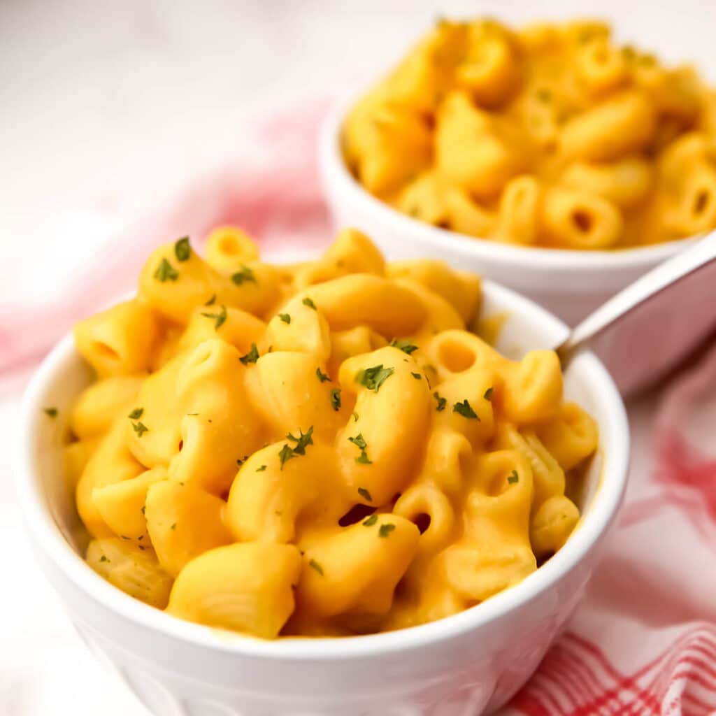 Two bowls of vegan pumpkin mac and cheese with a red and white tea towel on the side.