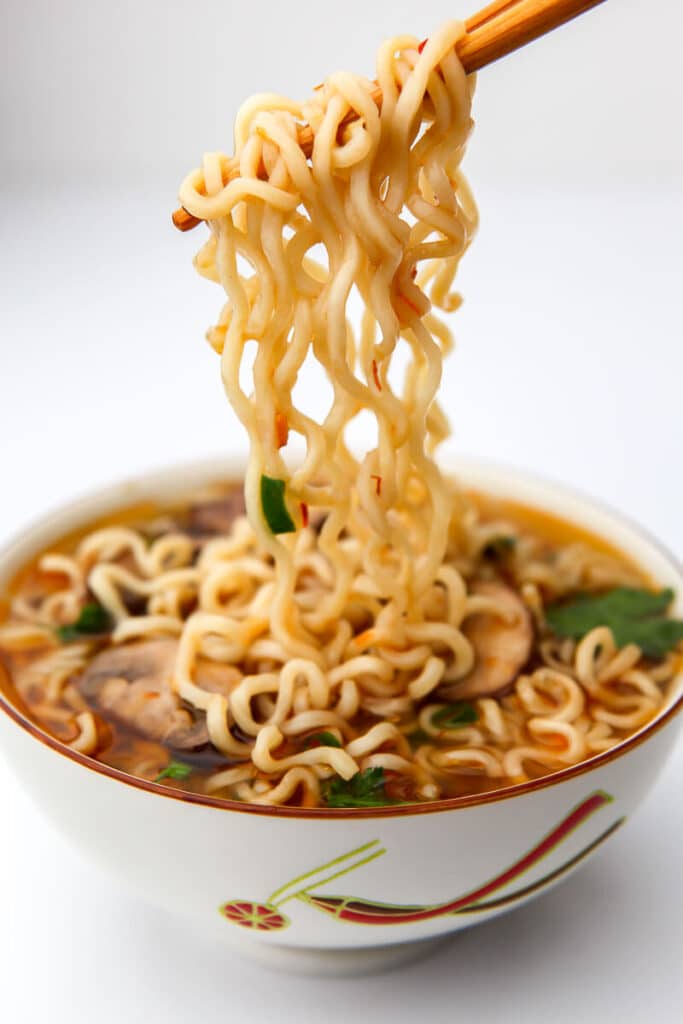 A bowl of ramen noodles with chop sticks holding some over the bowl.