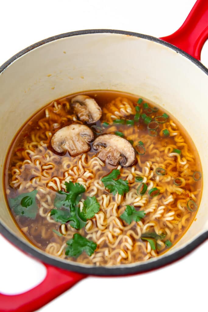 A small red saucepan filled with vegan ramen noodle soup.