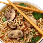 A close up top view of a bowl of vegan ramen with mushrooms and herbs on top.