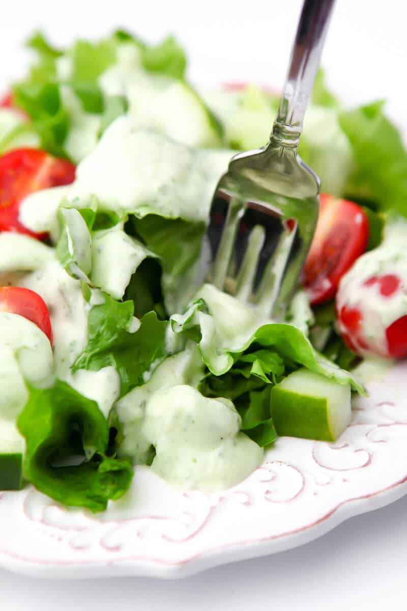 A white plate filled with salad drizzled with vegan ranch dressing with a fork sticking in it.