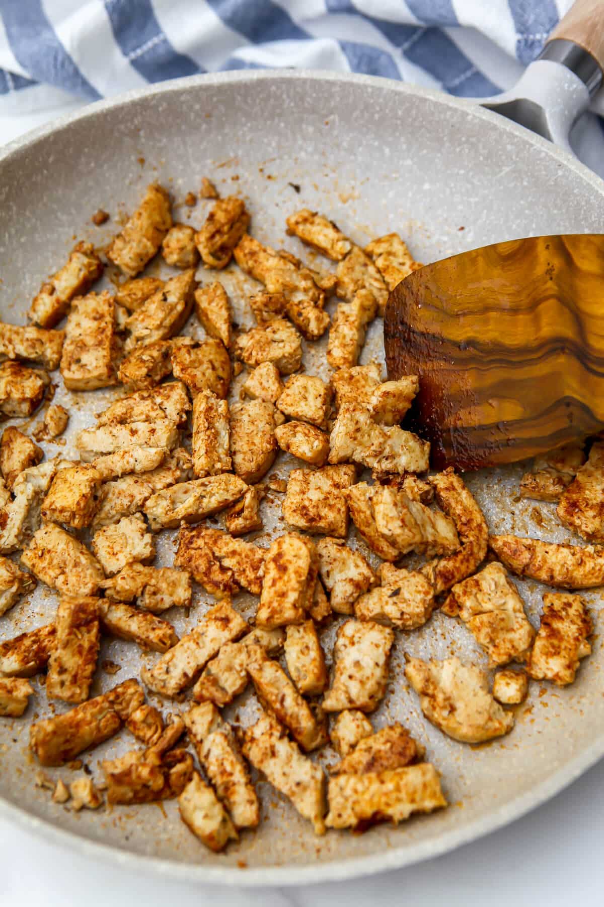 Vegan chicken strips sautéing in a pan with Jamaican jerk seasoning.