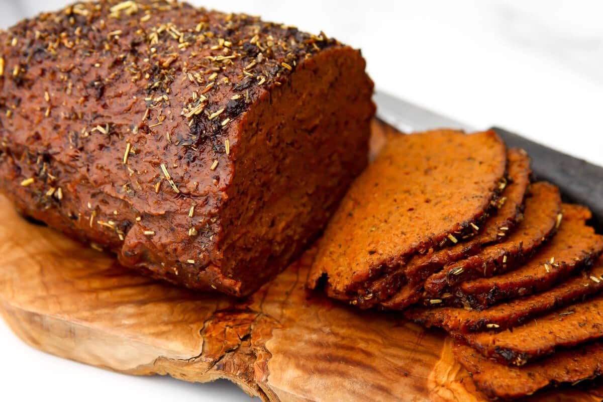 Vegan beef seasoned and baked into vegan roast beef that is sliced on a cutting board.