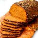 A vegan roast beef seasoned and sliced thin on a wooden cutting board.