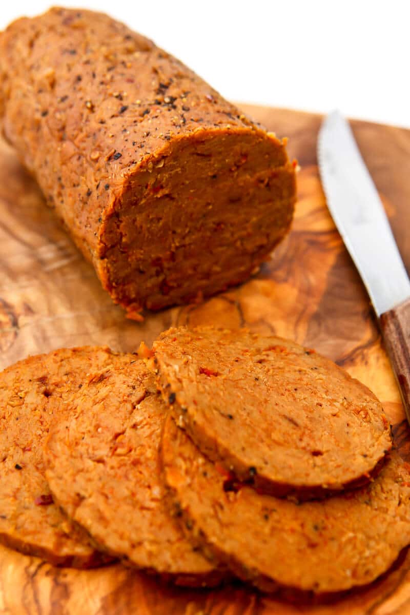 A log of vegan salami on a cutting board with some slices cut off of it.