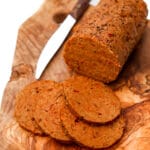 Vegan salami sliced on a cutting board with a knife next to it.