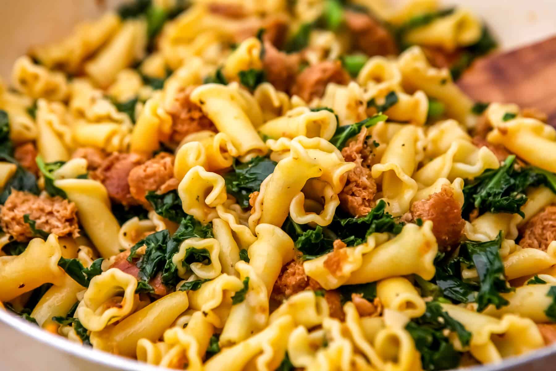 A large frying pan filled with vegan sausage pasta with garlic and kale.