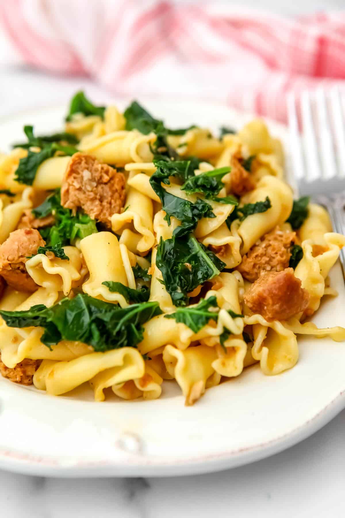 Vegan sausage pasta with kale on a white plate.