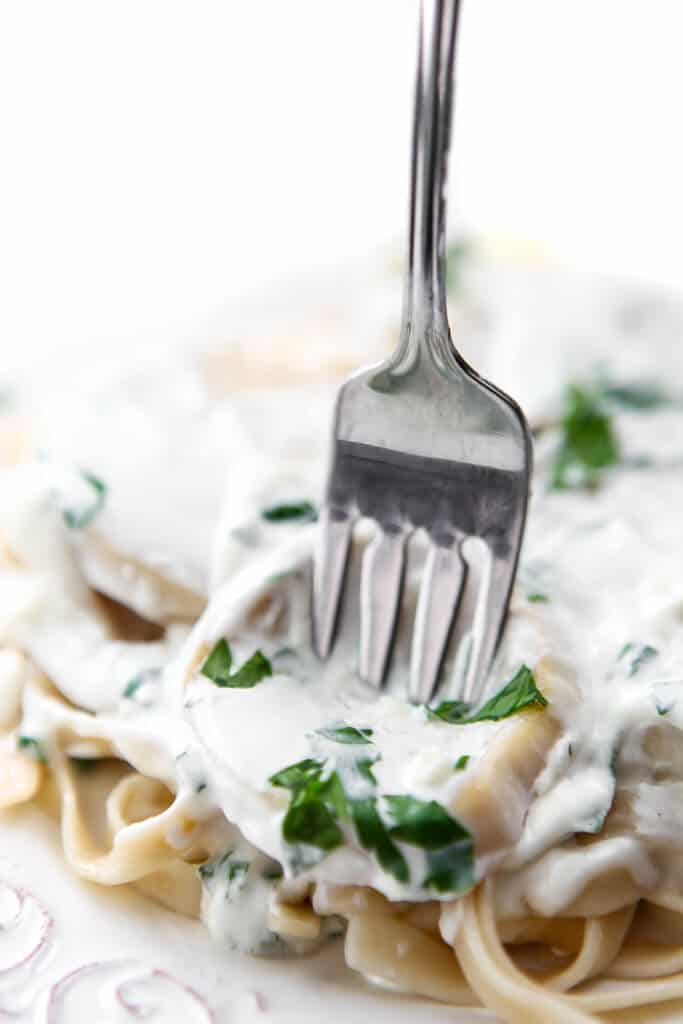 A close up of a slice of king mushroom over pasta with a fork in it.