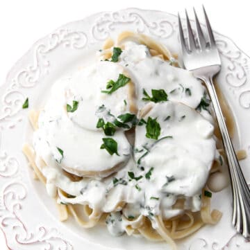 A white plate filled with linguine topped with vegan scallops and a garlic cream sauce garnished with parsley.