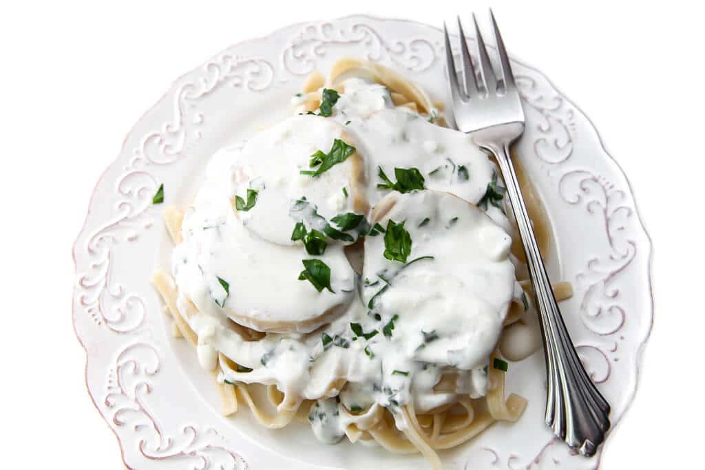 A plate full of king mushrooms in a garlic cream sauce over a bed of pasta.