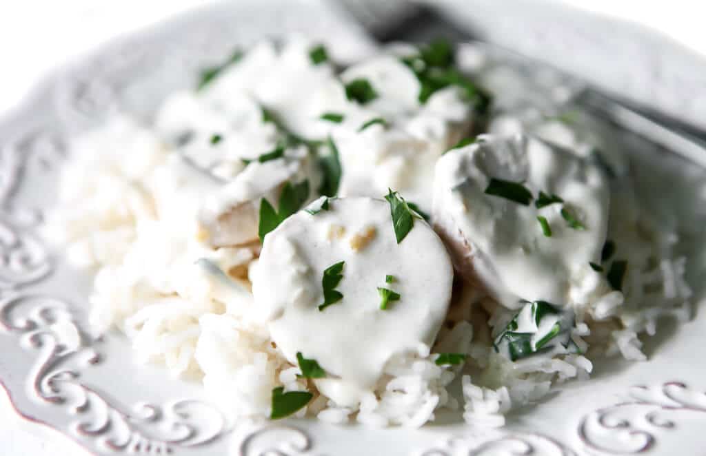 A white plate with a bed of rice topped with plant-based scallops made with king mushrooms in a garlic cream sauce.