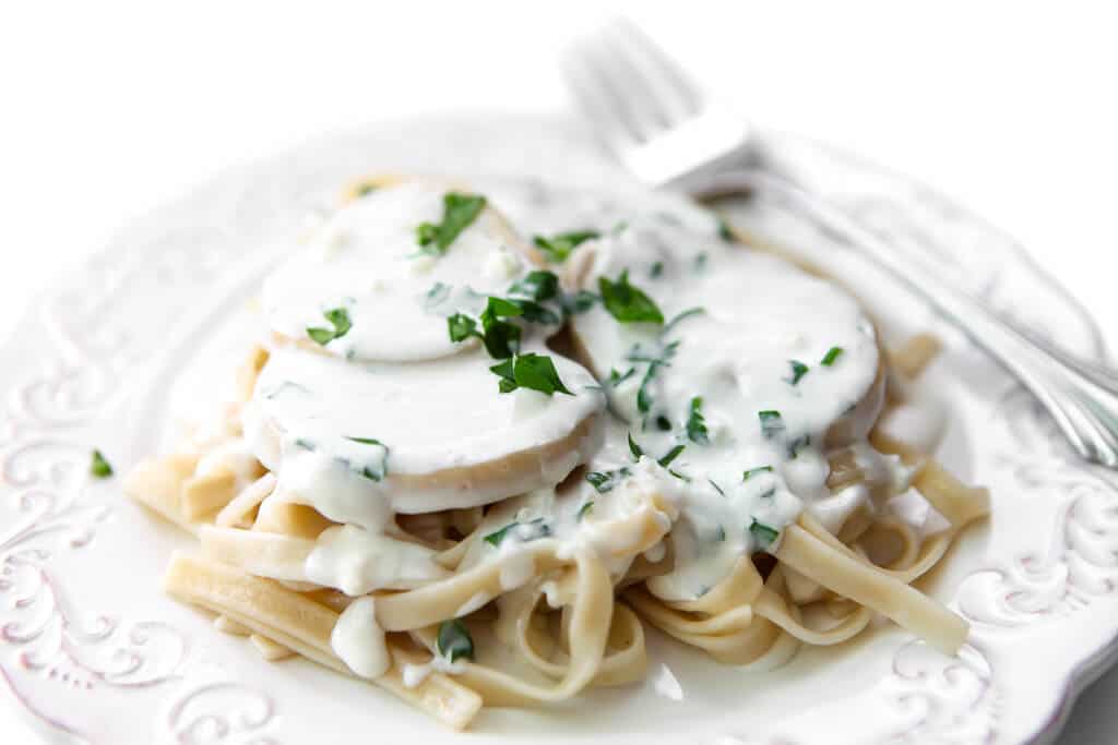 A plate full of sautéed king oyster mushrooms in a white sauce on a bed of pasta sprinkled with parsley.