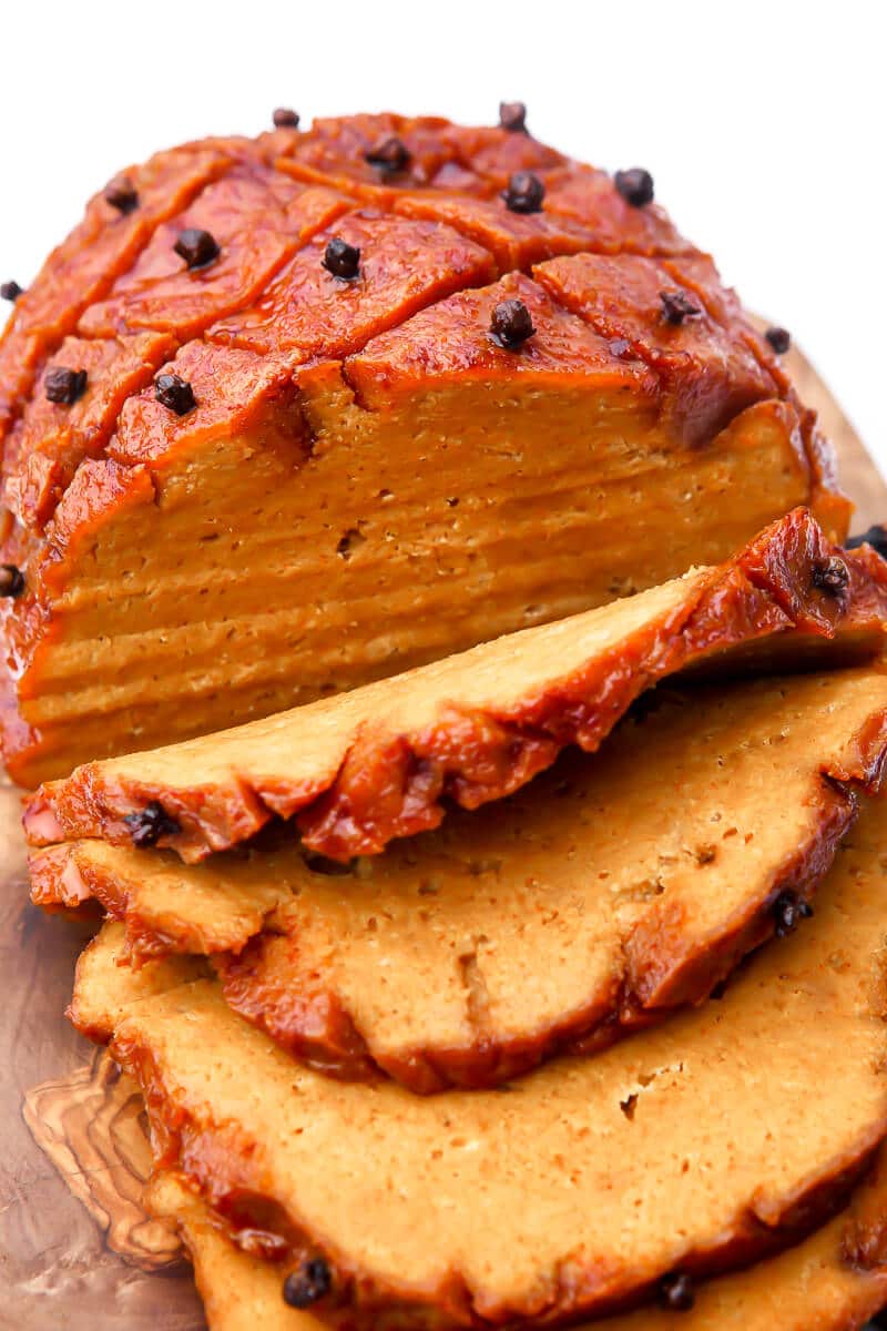 A roasted vegan ham sliced on a cutting board.