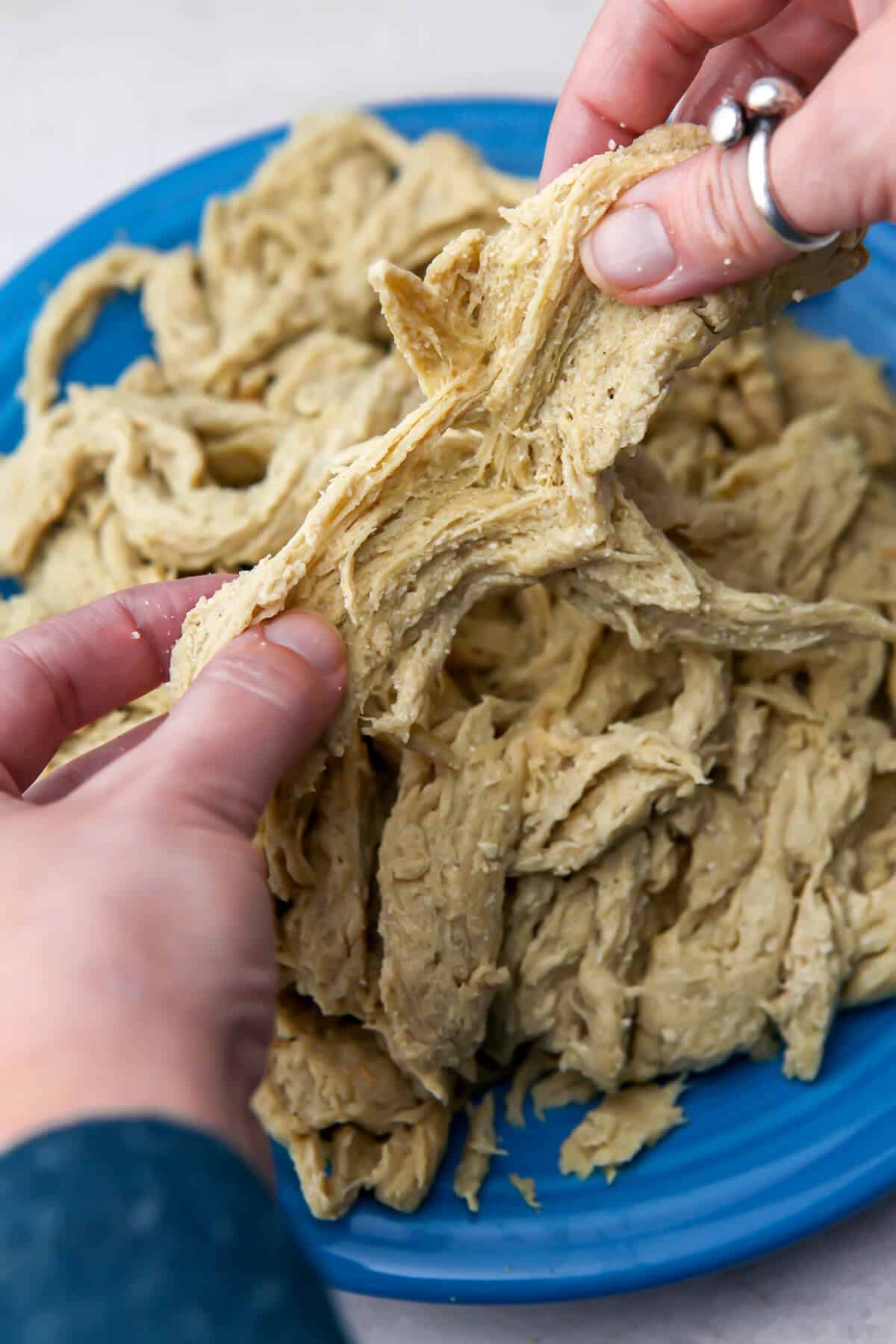 Someone pulling apart and shredding vegan chicken seitan.