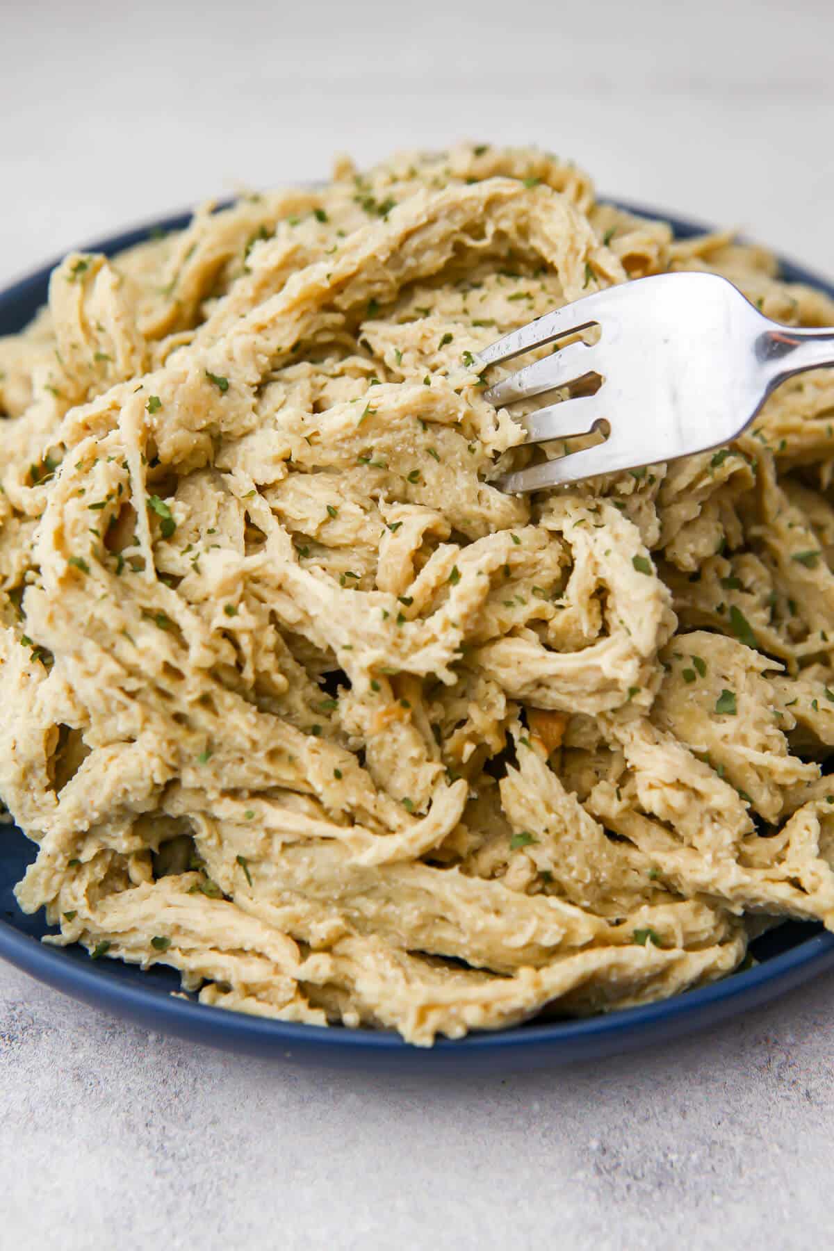 Vegan shredded chicken on a blue plate with a fork in it.