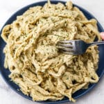 Vegan shredded chicken made from seitan on a blue plate with a fork in it.