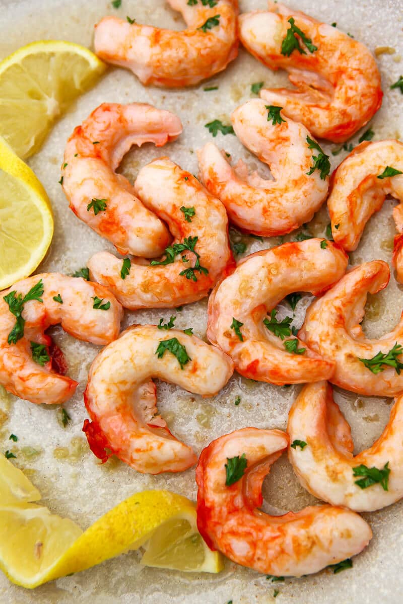 Vegan shrimp sauted in a pan with butter and garlic and sprinkled with fresh parsley and lemon wedges.