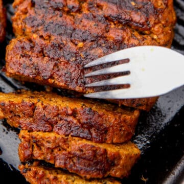 A vegan steak on an iron skillet cut into slices with a fork in it.