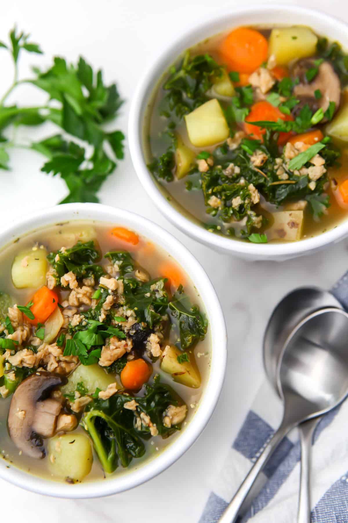 Two bowls of vegan stew with mushrooms, kale, potatoes, and TVP in it.