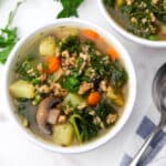 A bowl of vegan stew with mushrooms, kale, potatoes, and carrots.