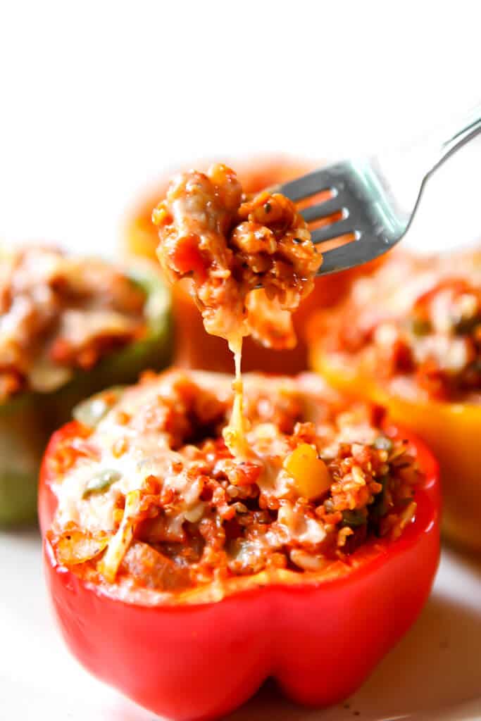 A red bell pepper stuffed with a vegan filling with a fork scooping some filling out.