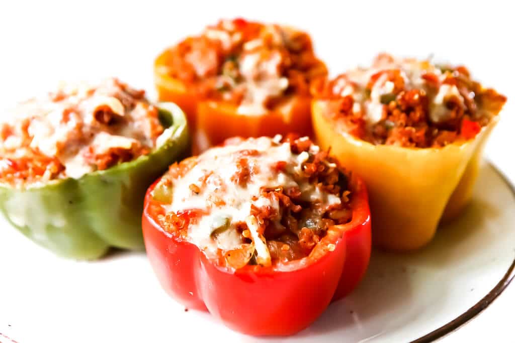 Four multi-colored vegan stuffed peppers topped with vegan cheese.