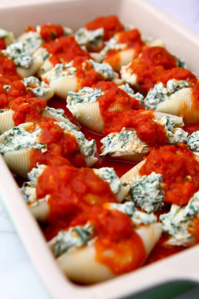 Vegan stuffed shells topped with tomato sauce before baking.