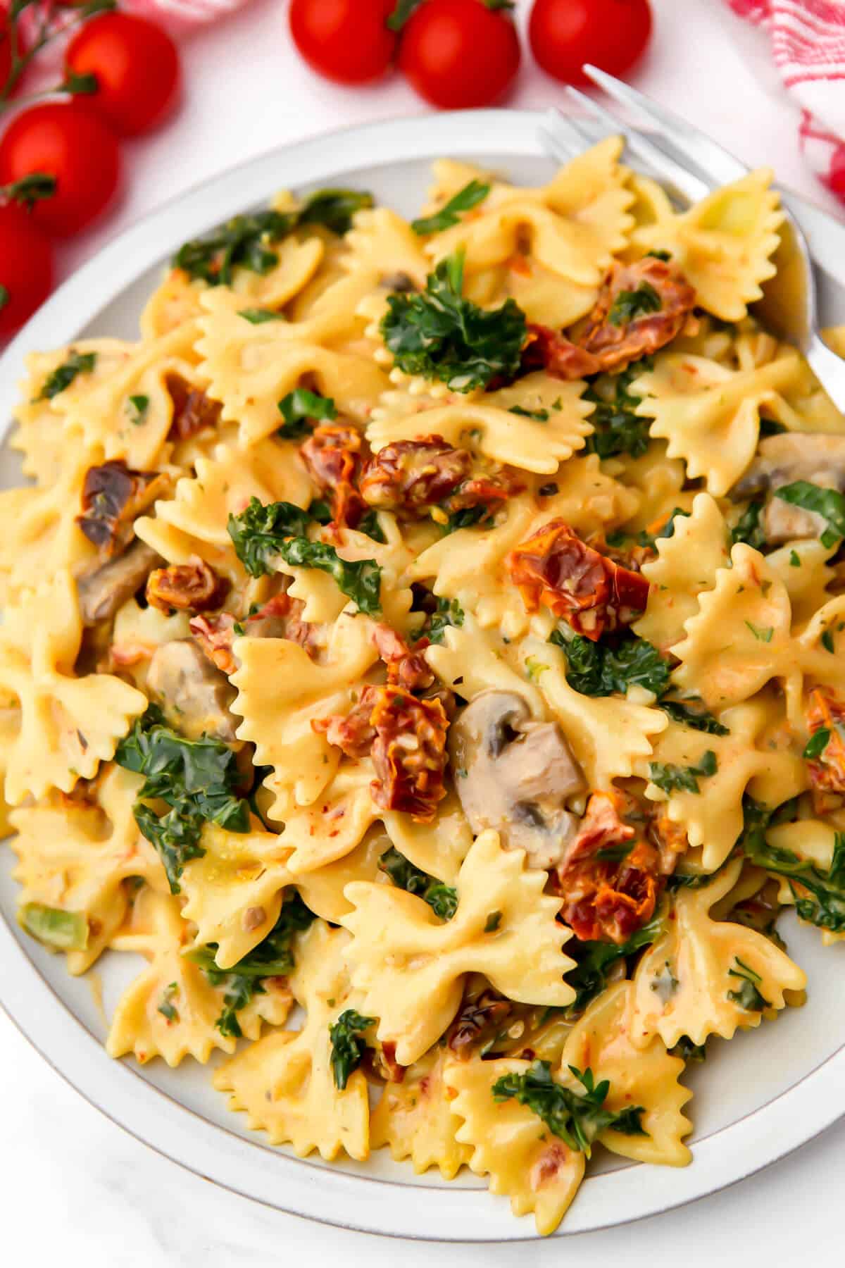 Vegan sundried tomato pasta on a white plate with cherry tomatoes around it.