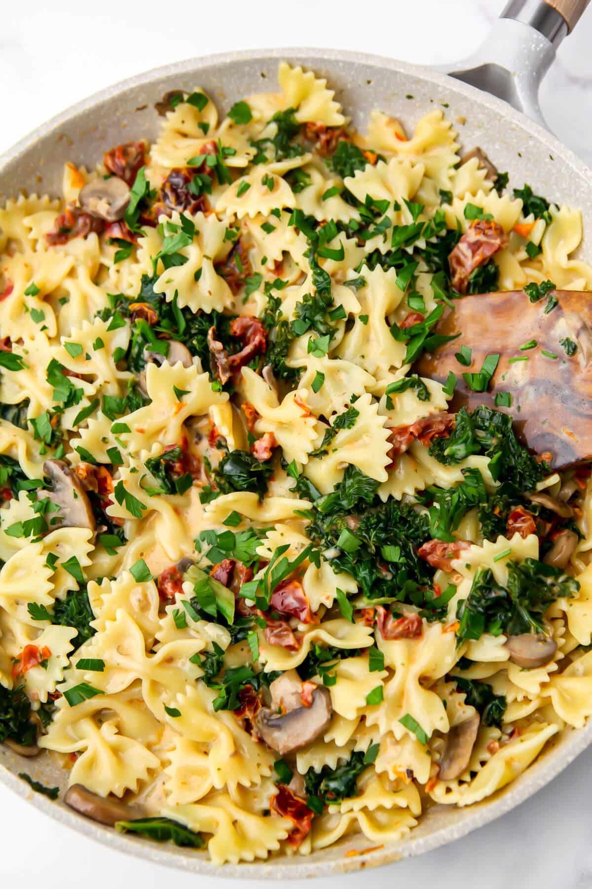 A frying pan full of vegan sundried tomato pasta with mushrooms and kale.