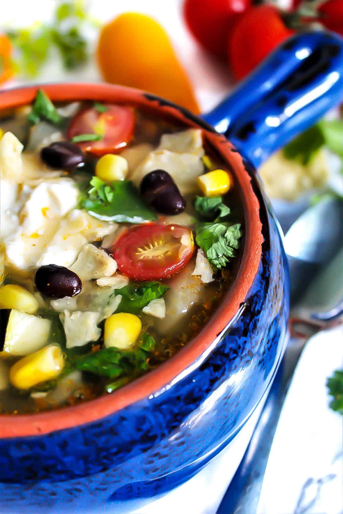 A blue bowl filled with vegan taco soup with beans and corn, topped with vegan sour cream.