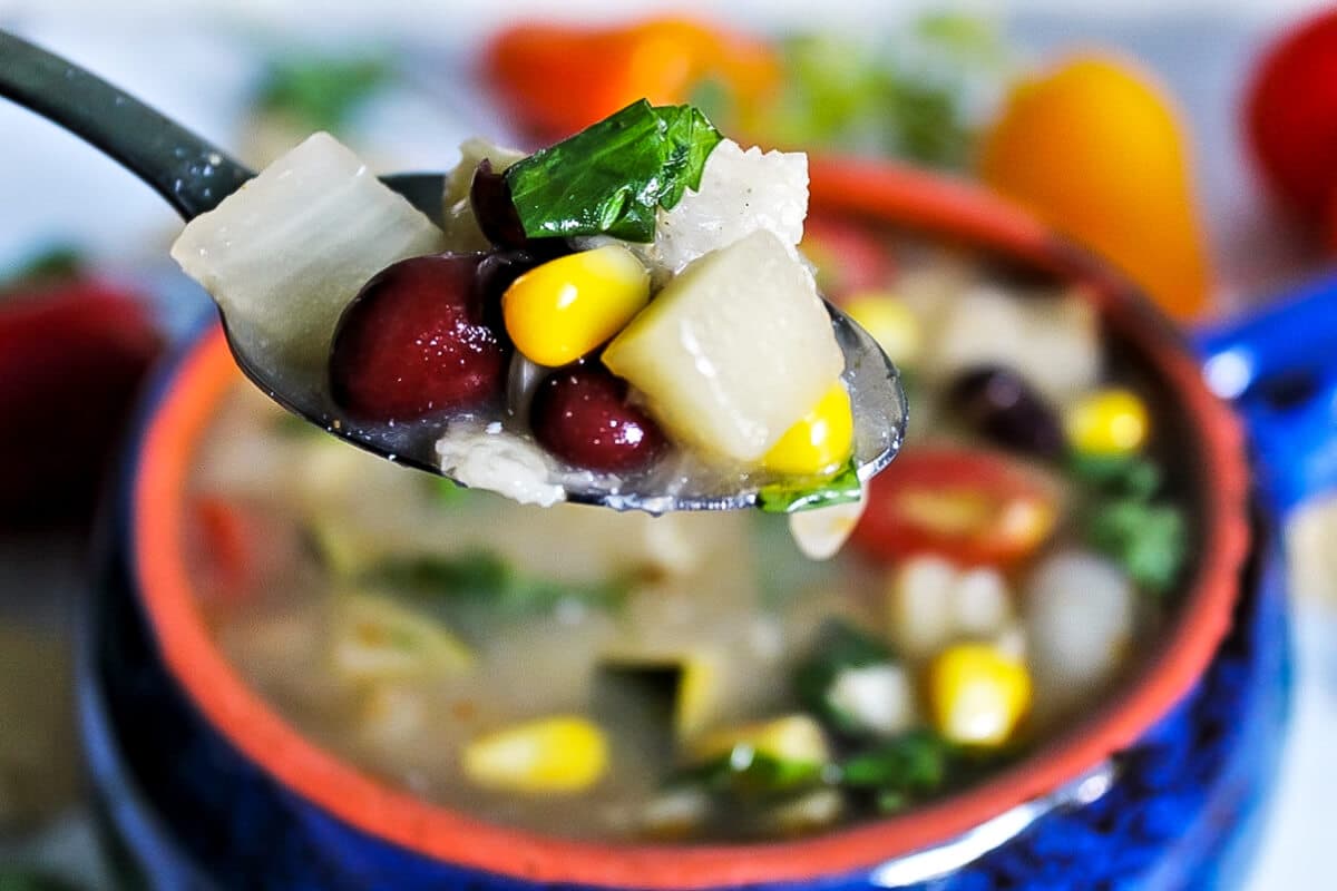 A spoonful of vegan taco soup with beans, corn, zucchini, and fresh cilantro.