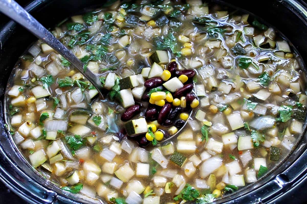 Vegan taco soup with corn and beans in a crock pot being scooped out by a ladle.