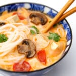 A blue bowl filled with creamy vegan tom kha soup with cherry tomatoes, tofu, mushrooms, and cilantro.