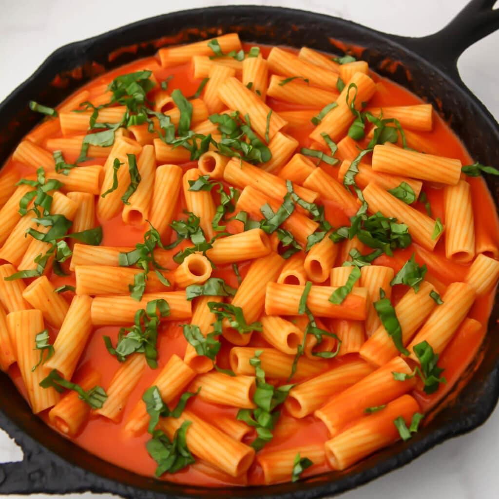 An iron skillet full of vegan vodka pasta topped with fresh basil.