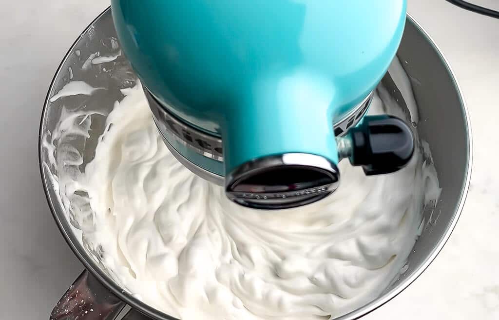Vegan whipped cream being whipped in a blue kitchen aid mixer.