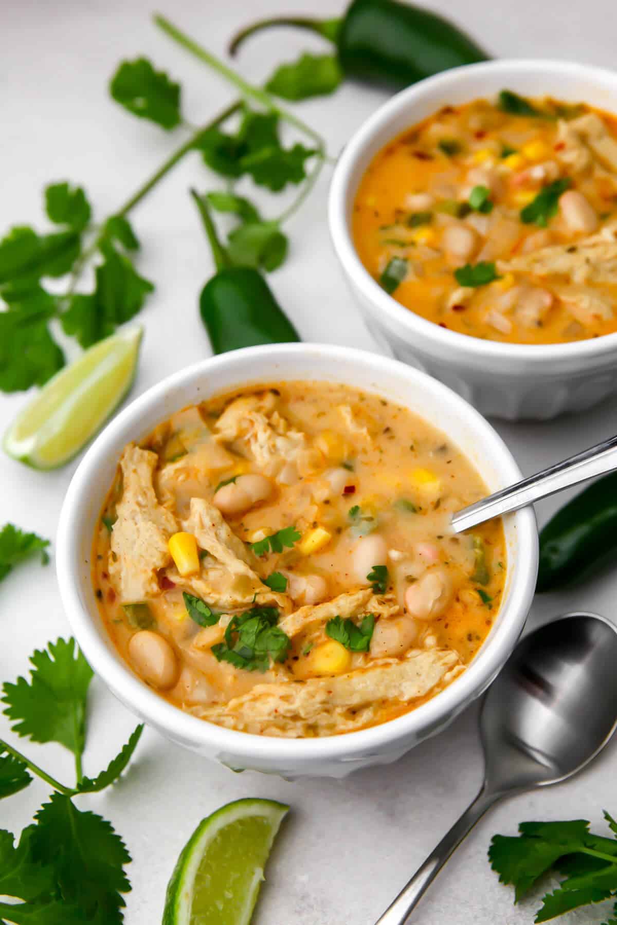 Two bowl of vegan white chili with cilantro and lime wedges around them.