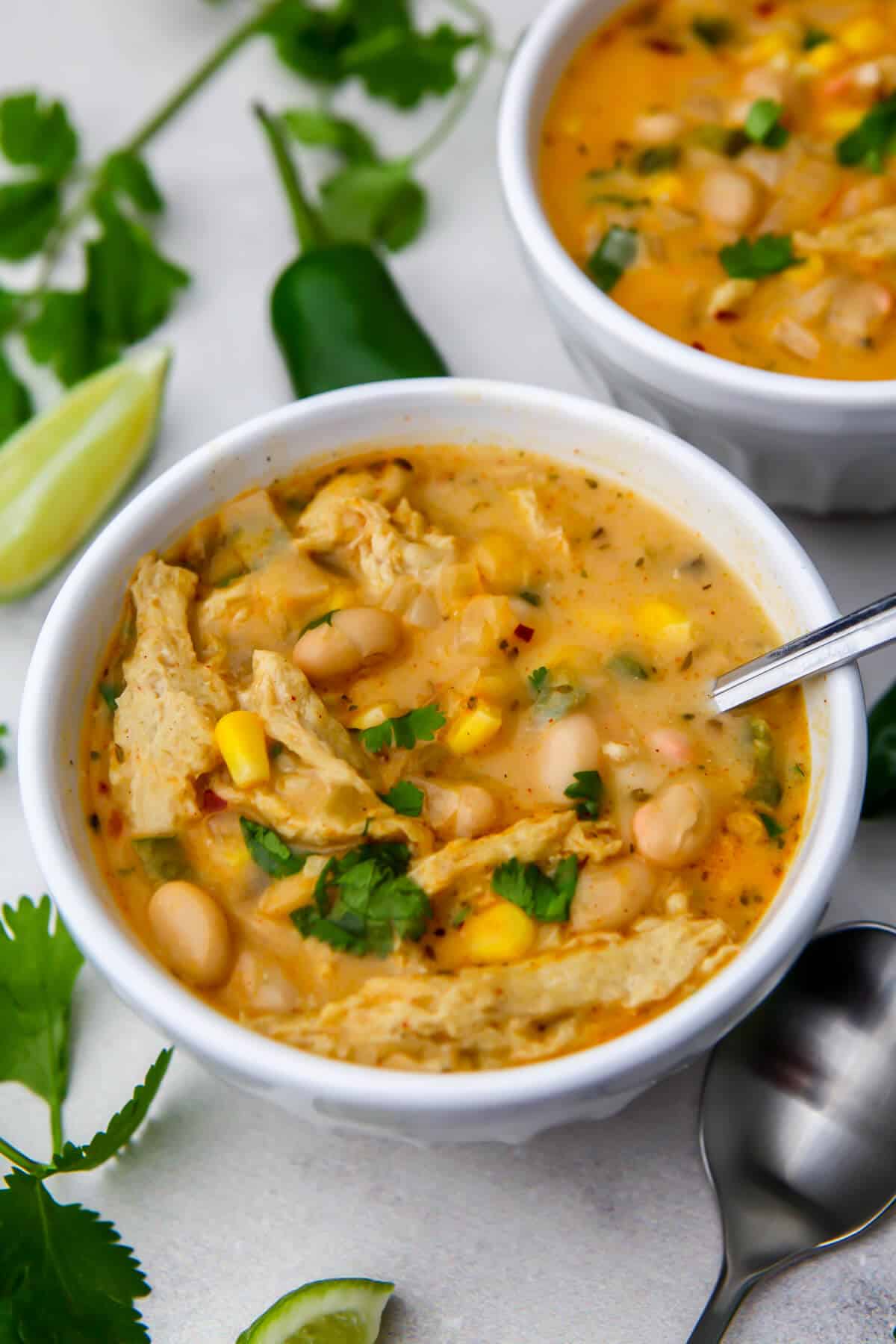 A bowl of dairy-free white chili with vegan chicken in it with cilantro and lime wedges on the side.