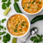 A top view of two bowls of vegan white chili with cilantro and jalapeno peppers on the side.