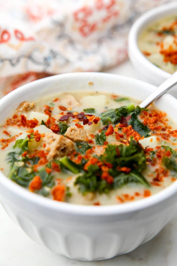 A bowl of vegan Zuppa Toscana with sausage, kale and vegan bacon bits with a tea towel behind it.