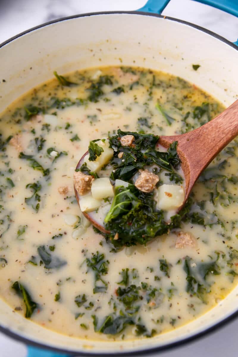 Meat free and dairy free Zuppa Toscana being scooped out of a pot with a wooden ladel.