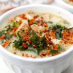 A white bowl filled with Zuppa Toscana with a tea towel behind it.