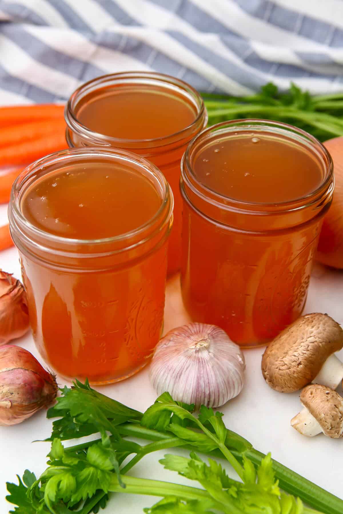 Three jars of homemade vegetable broth with vegies around them.